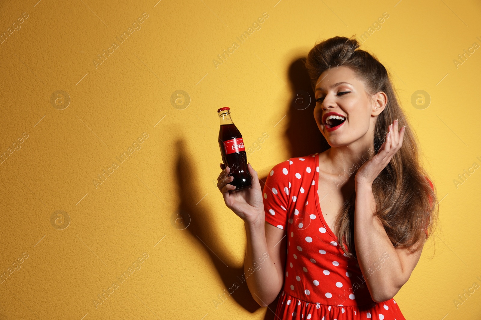 Photo of MYKOLAIV, UKRAINE - NOVEMBER 28, 2018: Young woman with bottle of Coca-Cola on color background, space for text