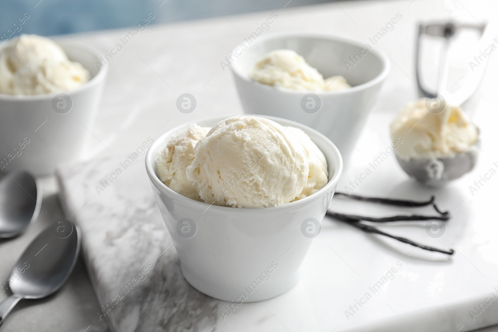 Photo of Bowls with tasty vanilla ice cream on marble board