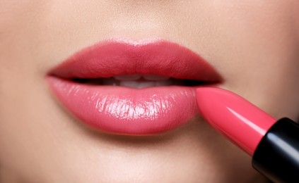 Young woman applying beautiful glossy lipstick, closeup