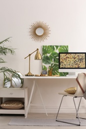 Photo of Modern workplace with computer and golden decor on desk near wall. Stylish interior design