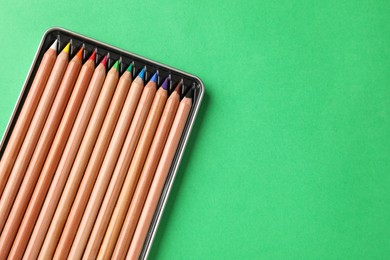 Photo of Box with many colorful pastel pencils on green background, top view and space for text. Drawing supplies