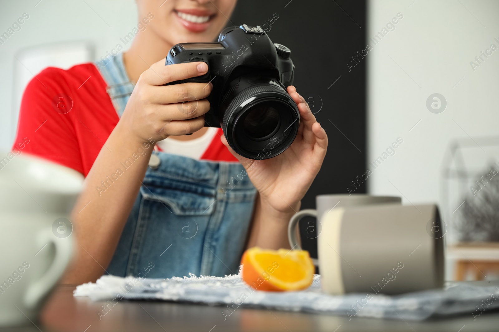 Photo of Young photographer taking picture of cups at table indoors, closeup