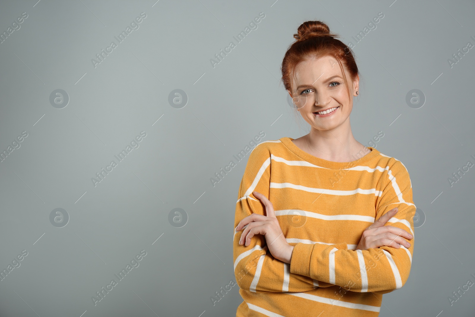 Photo of Candid portrait of happy red haired woman with charming smile on grey background, space for text