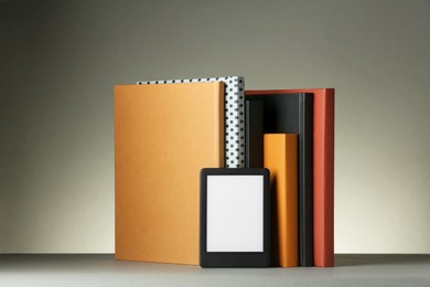 Modern e-book reader and hard cover books on light grey table