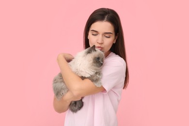 Photo of Woman kissing her cute cat on pink background