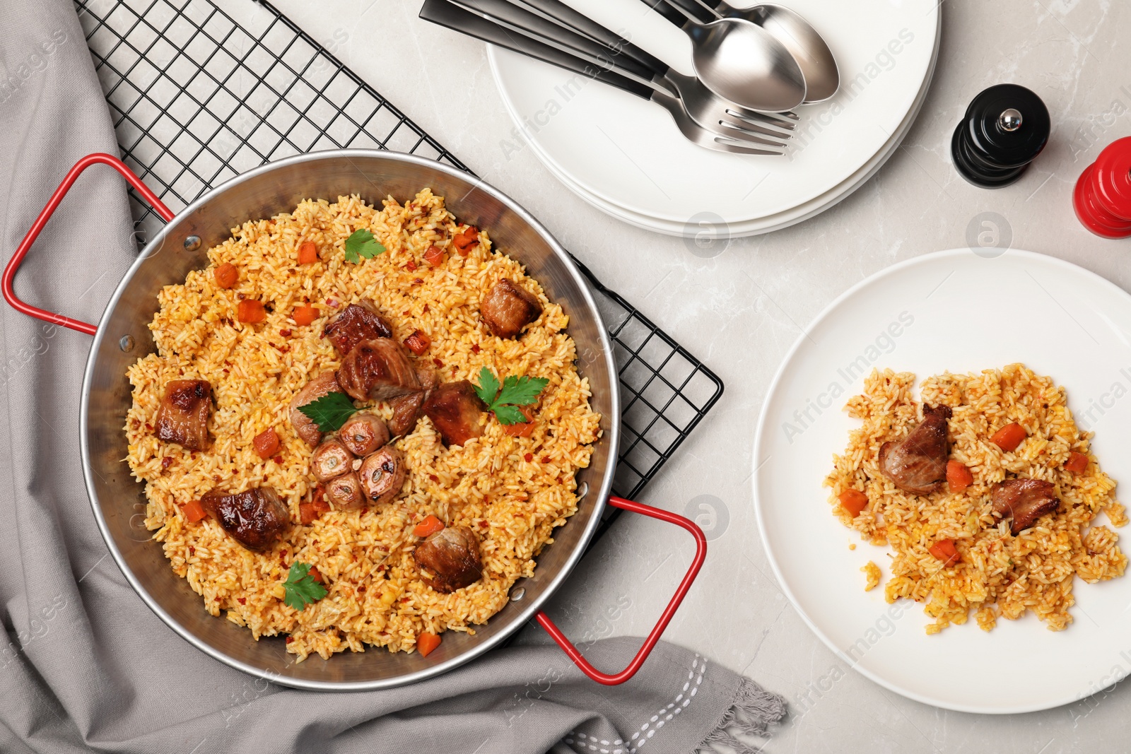 Photo of Frying pan and plate with delicious rice pilaf on light table, flat lay