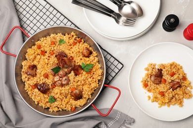 Frying pan and plate with delicious rice pilaf on light table, flat lay