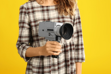 Photo of Woman with vintage video camera on yellow background, closeup