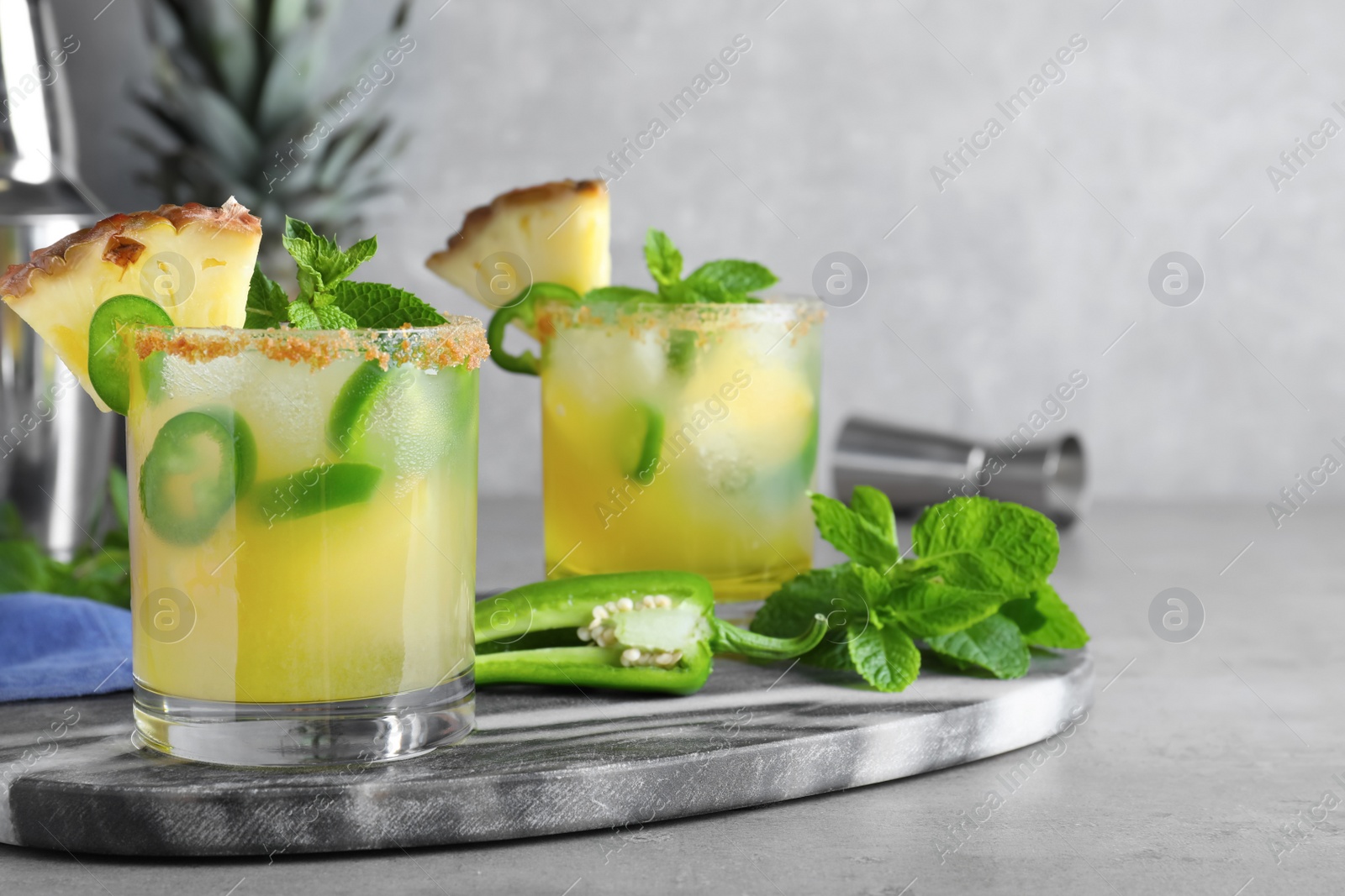 Photo of Glasses of spicy pineapple cocktail with jalapeno and mint on grey table. Space for text