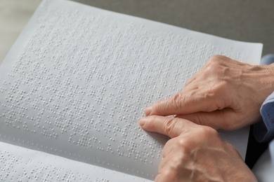 Photo of Blind senior person reading book written in Braille, closeup