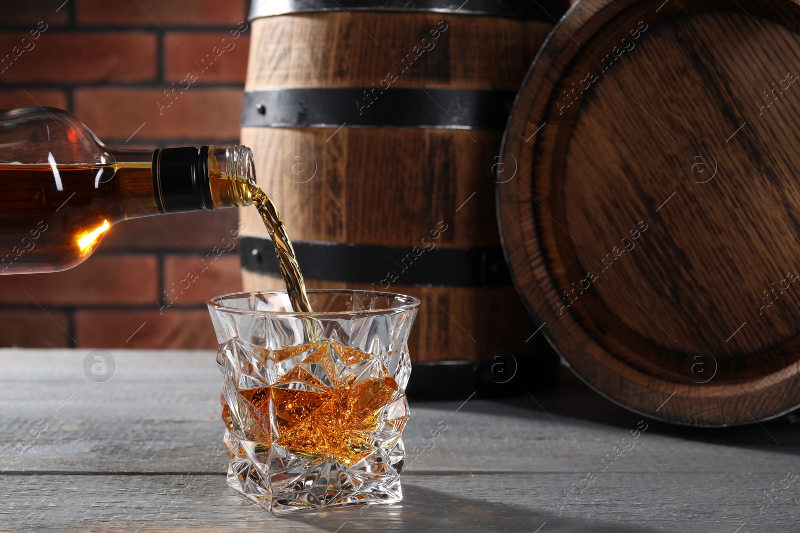 Photo of Pouring whiskey from bottle into glass on grey wooden table. Space for text