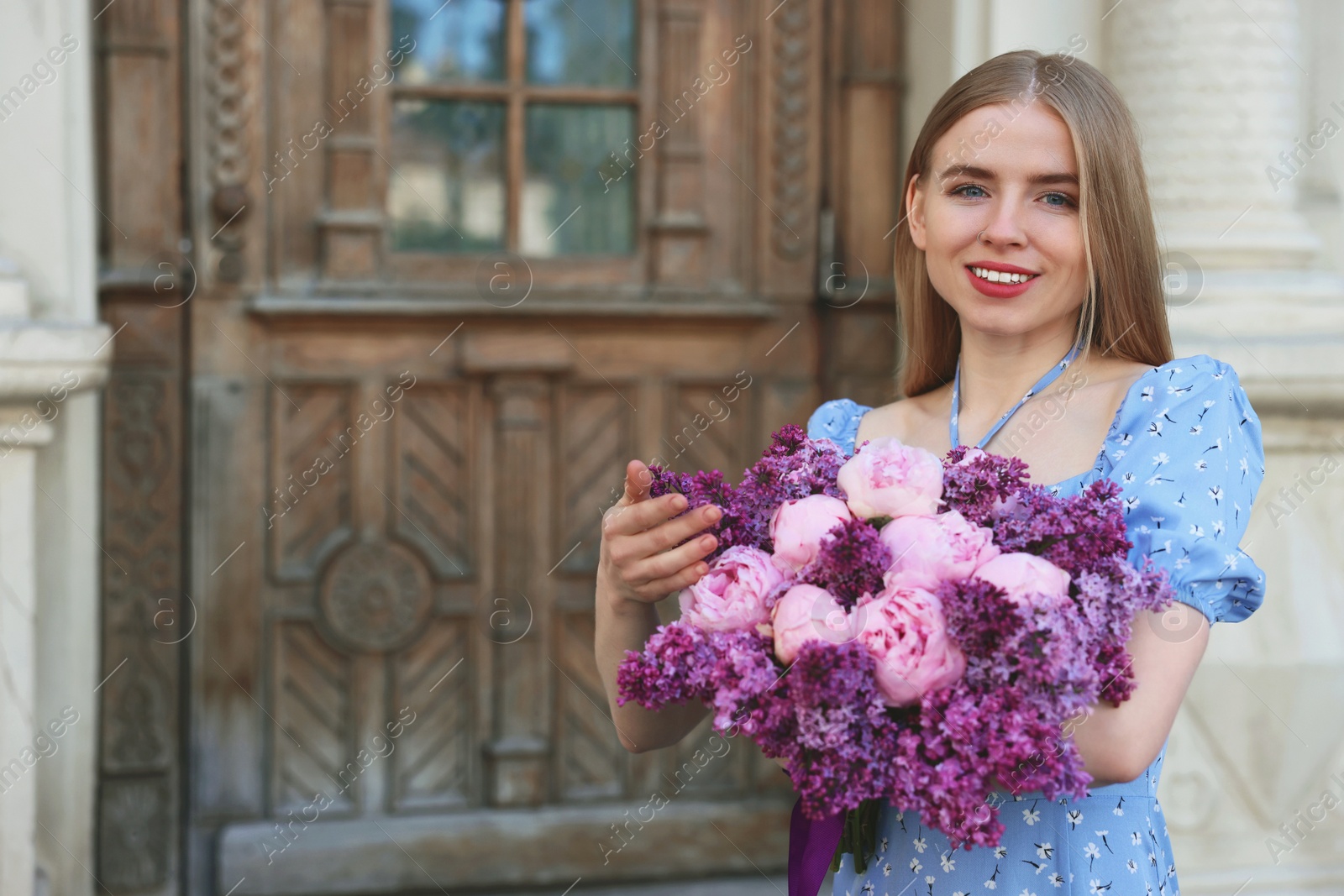 Photo of Beautiful woman with bouquet of spring flowers near building outdoors, space for text