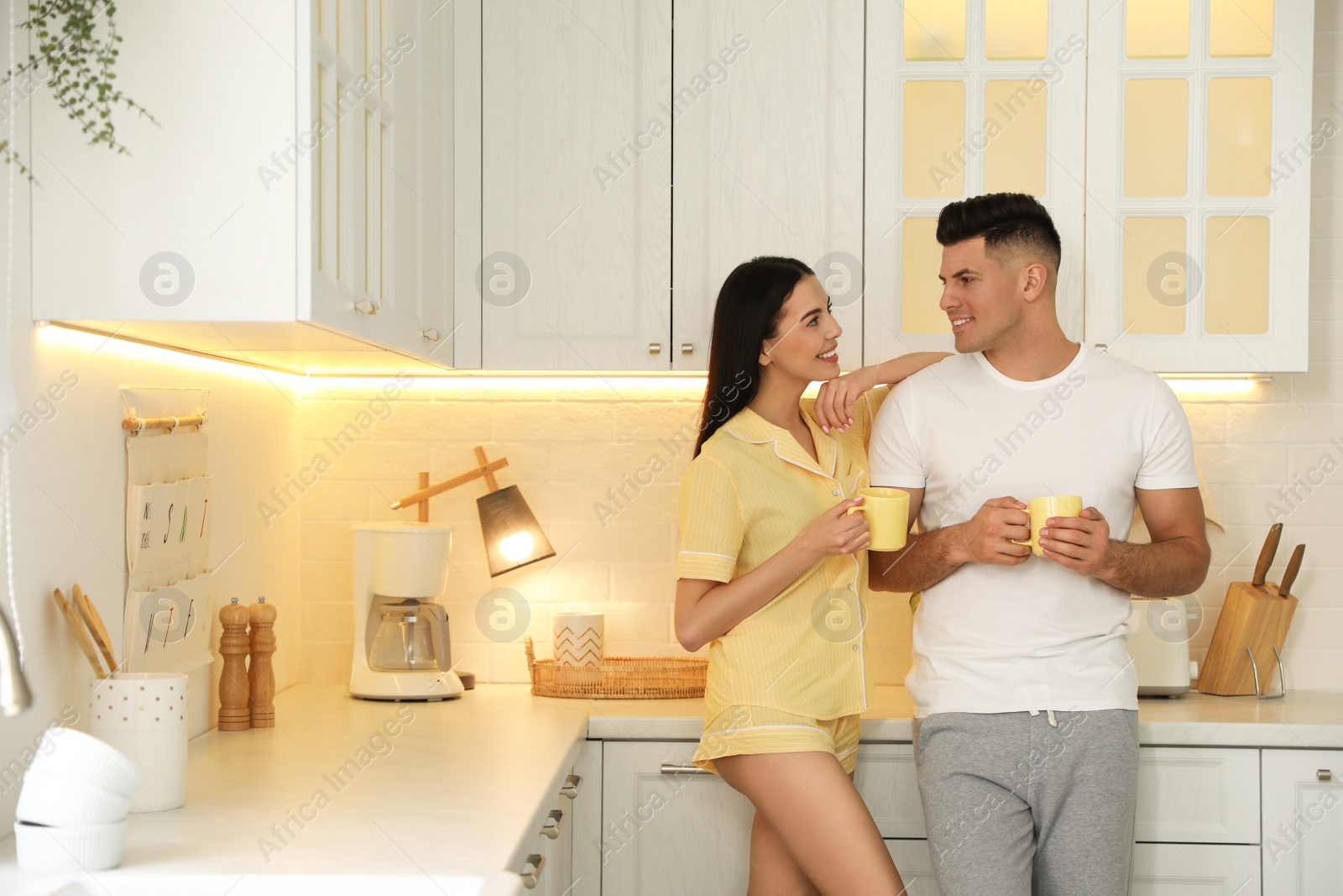 Photo of Happy couple wearing pyjamas with cups of coffee in kitchen