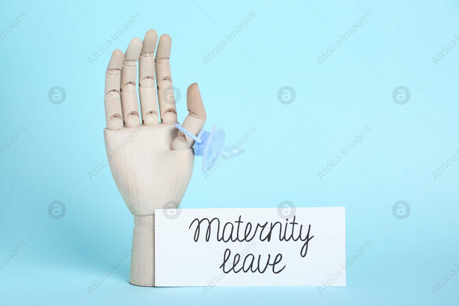 Photo of Wooden mannequin hand, pacifier and card with phrase Maternity Leave on light blue background. Space for text