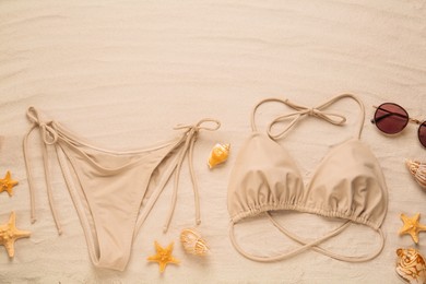 Photo of Stylish bikini, sunglasses, starfishes and shells on sand, flat lay. Space for text