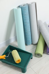 Different wallpaper rolls, roller and tray near white wall indoors