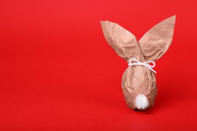 Photo of Easter bunny made of kraft paper and egg on red background. Space for text