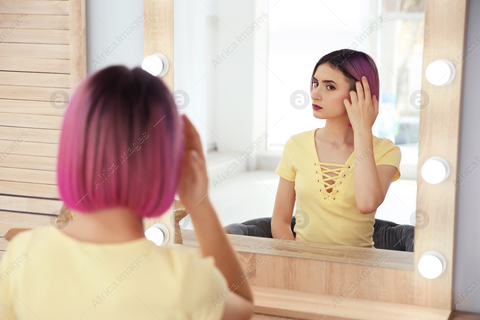 Photo of Young woman with color hair looking into mirror in beauty salon. Modern trend