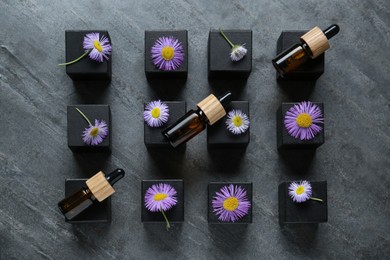 Photo of Flat lay composition with bottles of essential oil and beautiful flowers on dark gray stone table