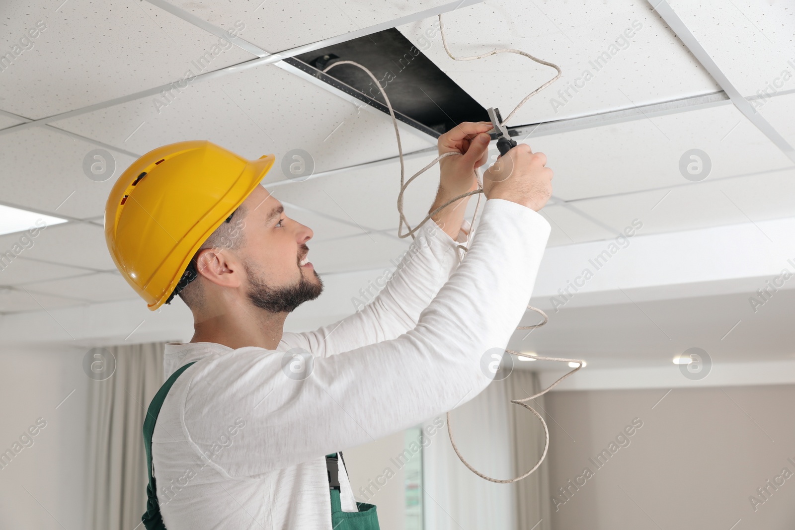 Photo of Electrician with pliers repairing ceiling wiring indoors