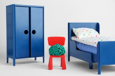 Brain made of plasticine on chair and mini furniture against white background