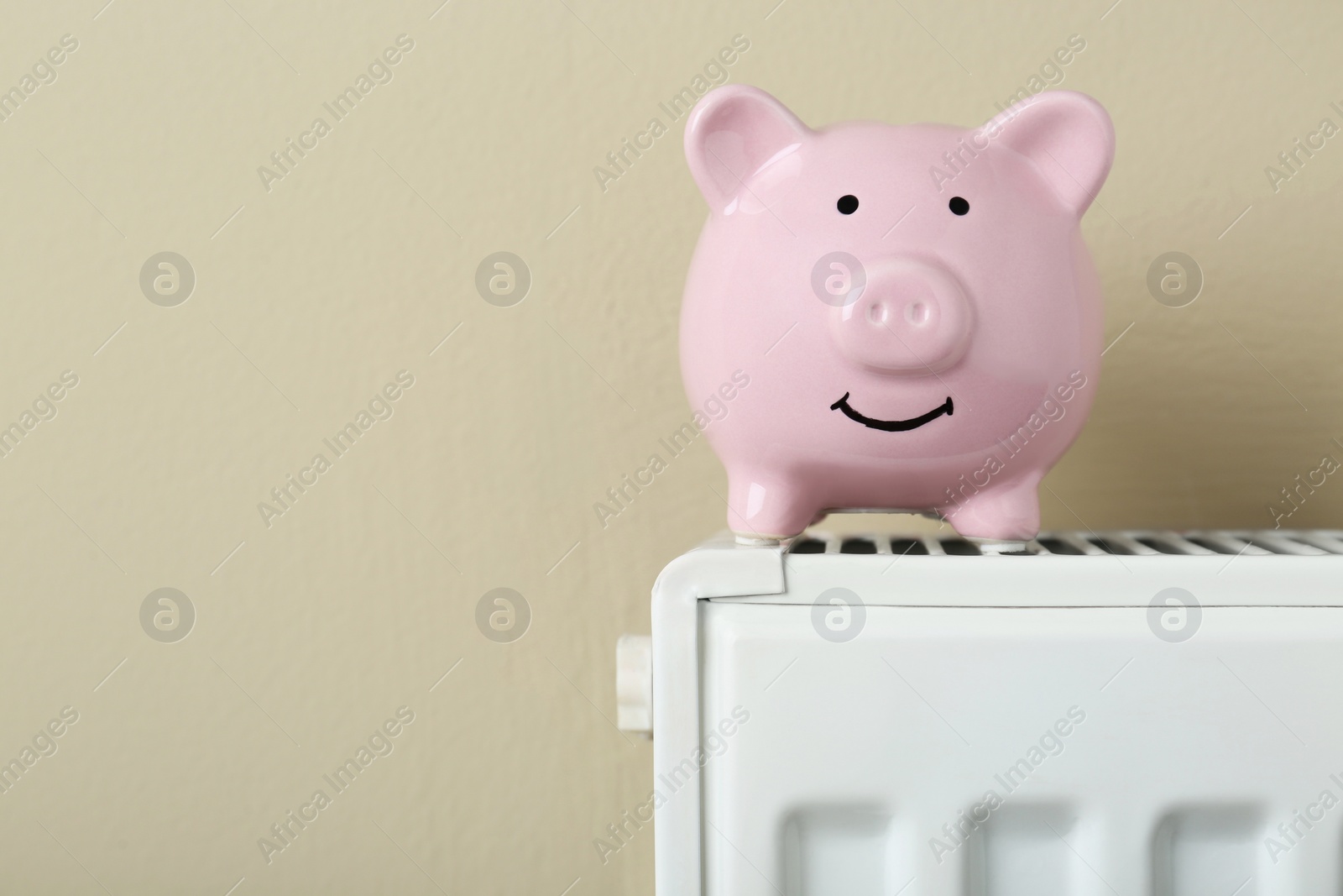 Photo of Piggy bank on heating radiator against beige background, space for text