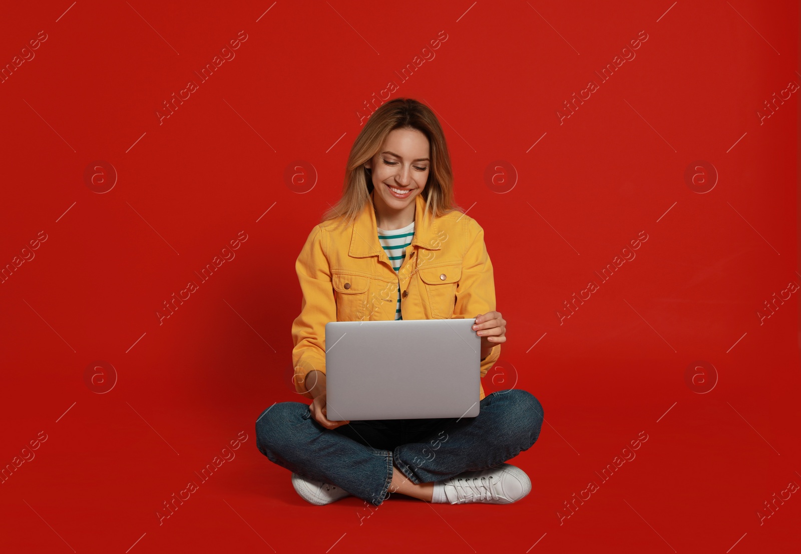 Photo of Young woman with modern laptop on red background