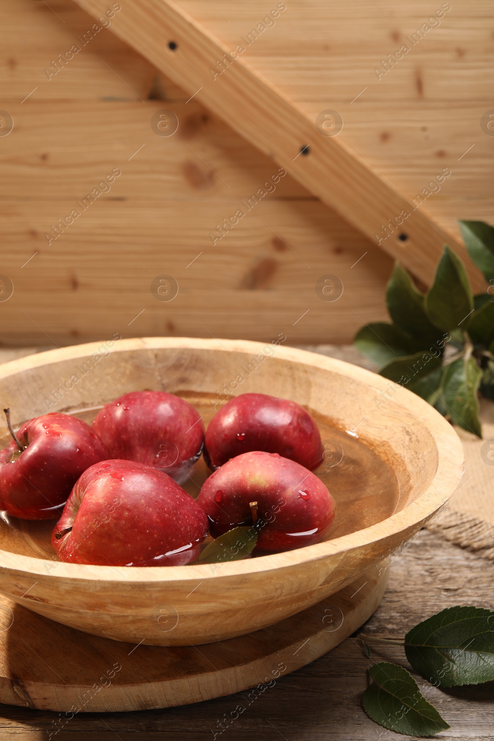 Photo of Fresh red apples in bowl with water on wooden table