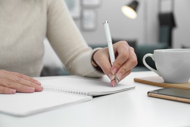 Left-handed woman writing in notebook at table indoors, closeup