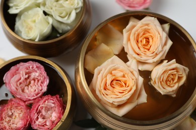 Photo of Tibetan singing bowls with water and different beautiful rose flowers on white background, above view