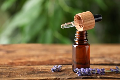 Bottle of lavender essential oil and flowers on wooden table against blurred background. Space for text