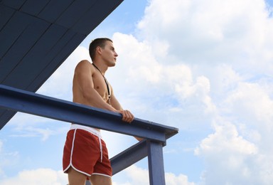 Handsome lifeguard on watch tower against sky