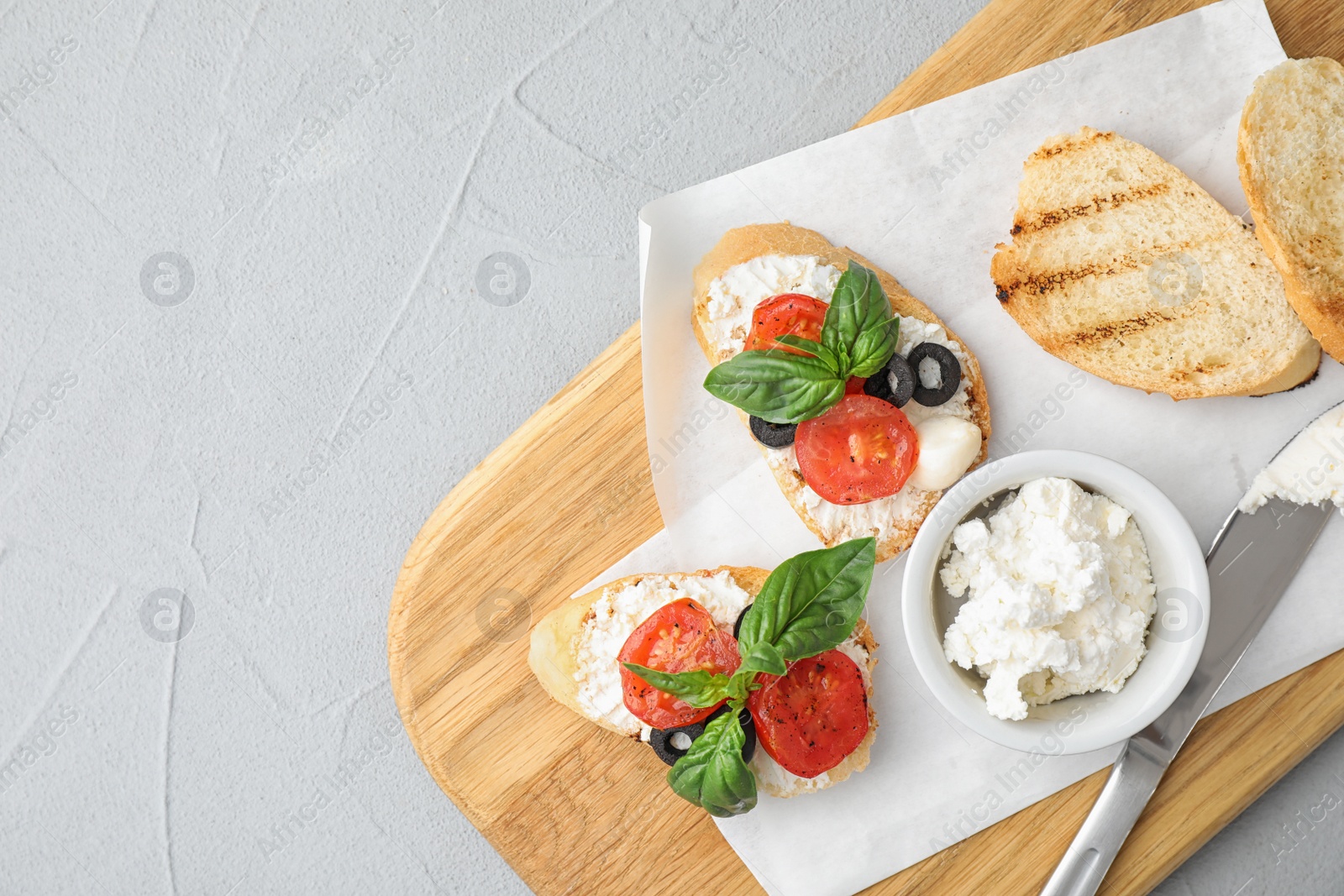 Photo of Wooden board with delicious tomato bruschettas on light grey background, top view. Space for text