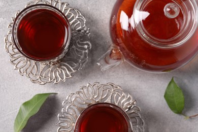 Photo of Glasses of traditional Turkish tea in vintage holders and pot on light grey table, flat lay