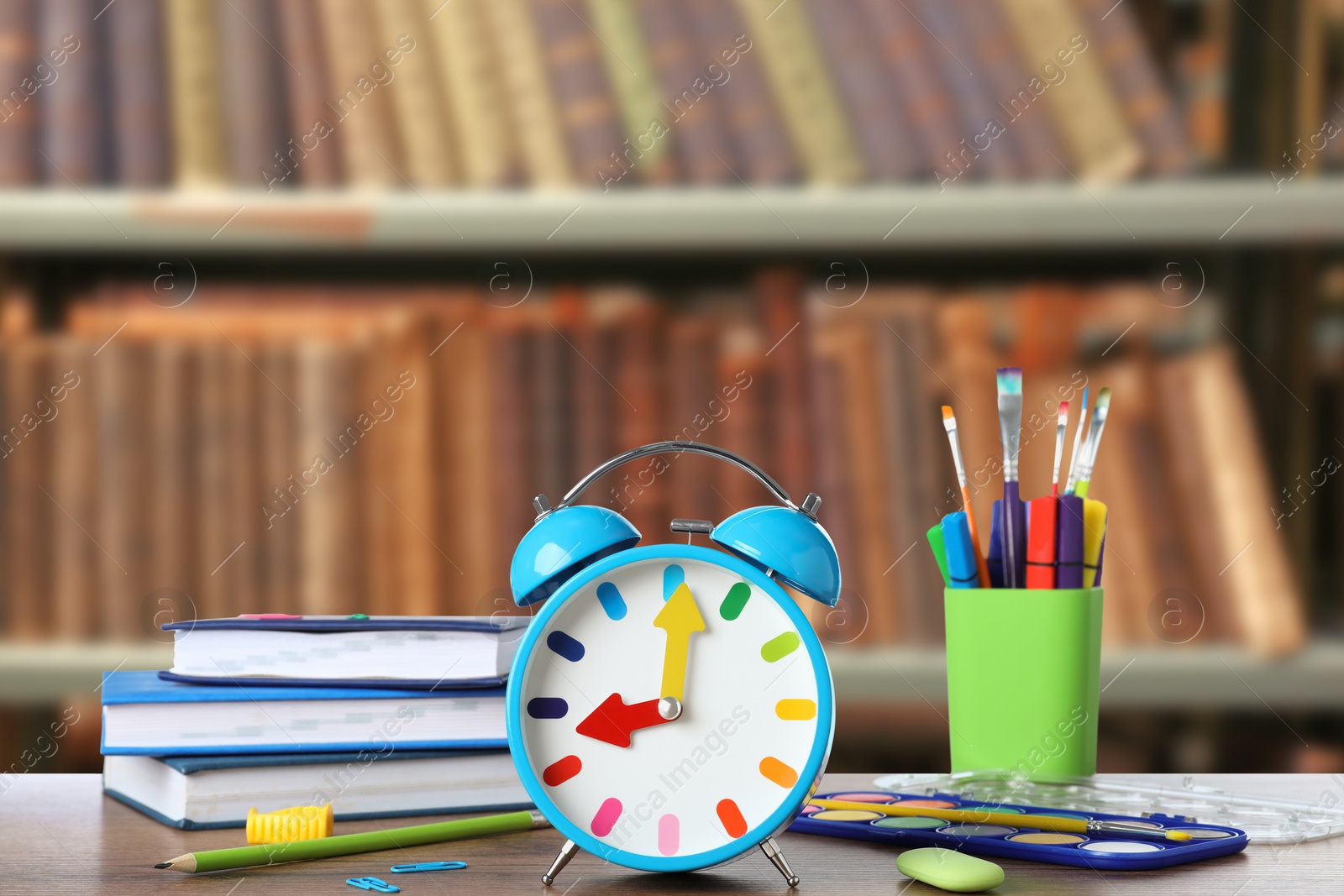 Image of Light blue alarm clock and different stationery on wooden table in library