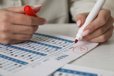 Photo of School grade. Teacher writing letter A with plus symbol on answer sheet at white table, closeup