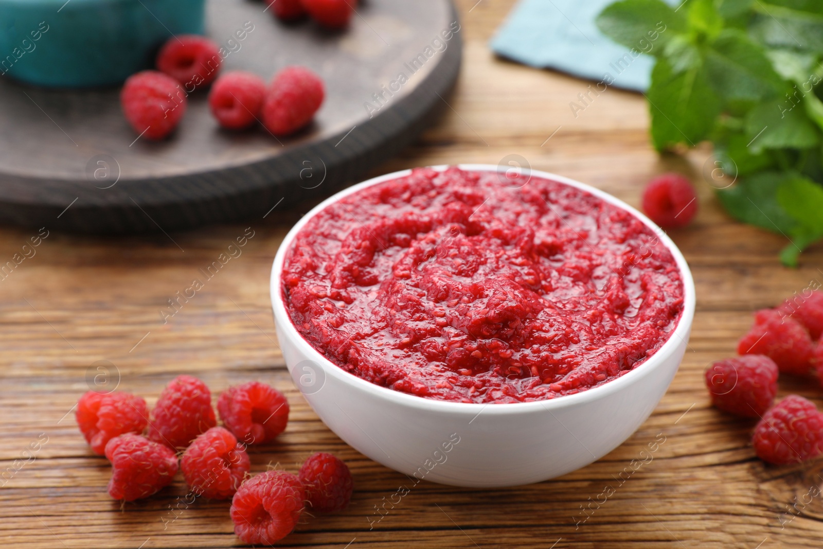 Photo of Raspberry puree in bowl and fresh berries on wooden table, closeup