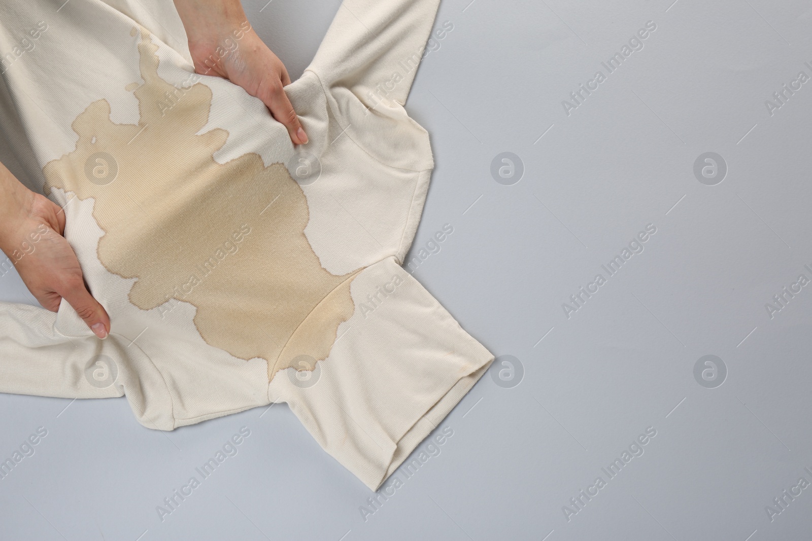 Photo of Woman holding beige sweater with stain on light grey background, top view. Space for text