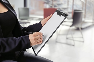 Psychologist with clipboard prepared for group therapy on blurred background, closeup. Space for text