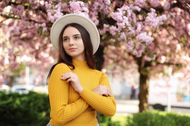 Beautiful woman in hat near blossoming tree on spring day, space for text