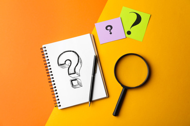 Flat lay composition of notebook, magnifier glass and cards with question marks on color background