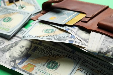 Photo of Many dollar banknotes with wallet and credit cards on green background, closeup