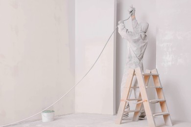 Decorator in uniform painting wall with sprayer indoors