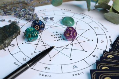 Photo of Zodiac wheel with sign triplicities, pen, gemstones and astrology dices on table, closeup