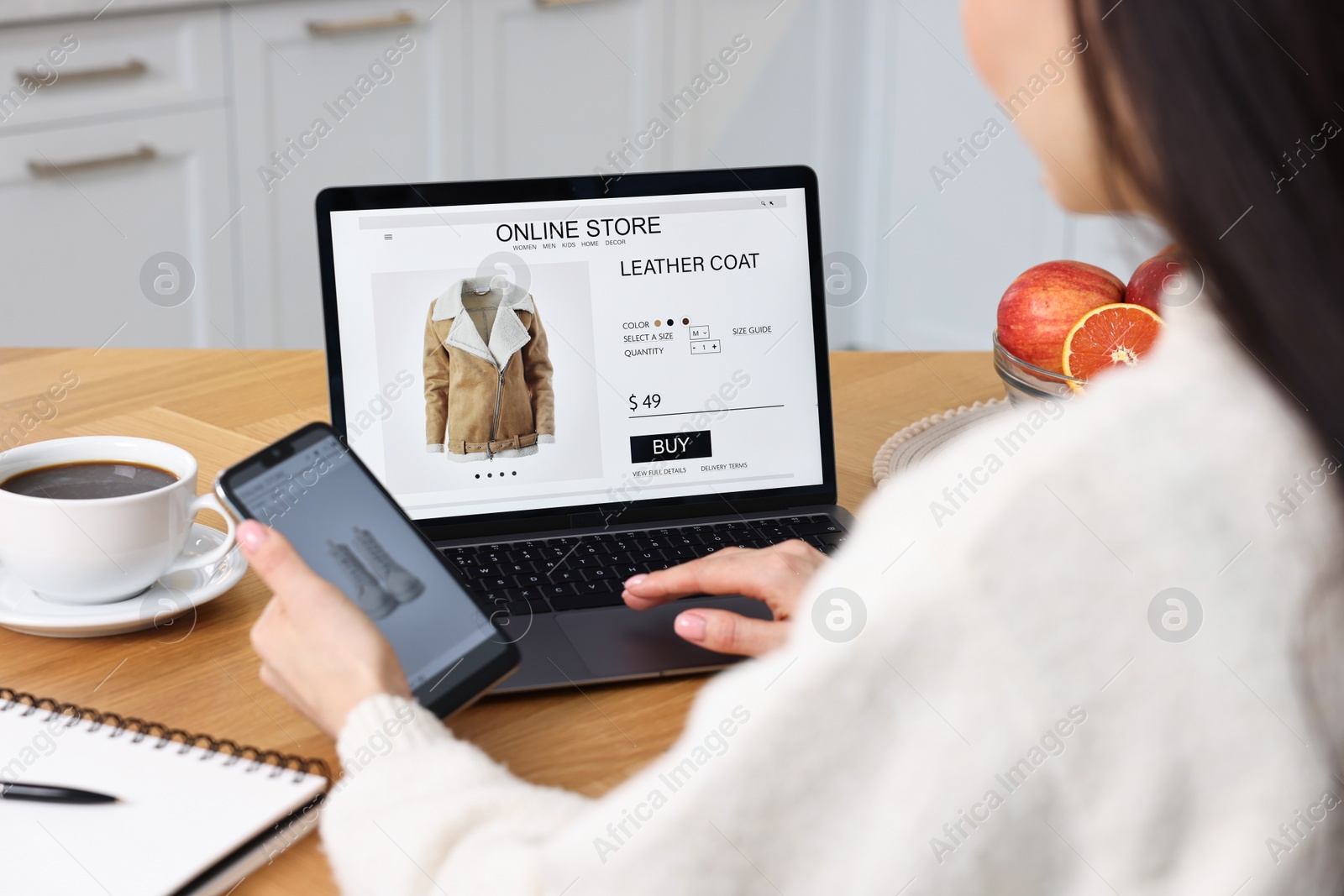 Photo of Woman with laptop and smartphone shopping online at wooden table in kitchen, closeup