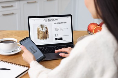 Photo of Woman with laptop and smartphone shopping online at wooden table in kitchen, closeup