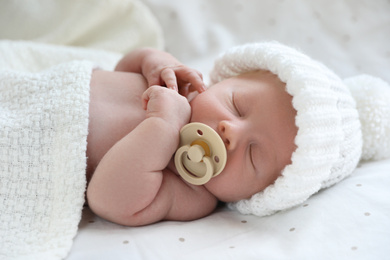 Photo of Cute newborn baby in white knitted hat lying on bed