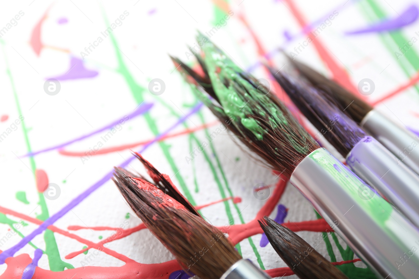 Photo of Brushes on canvas with colorful paint splashes, closeup. Art and creativity