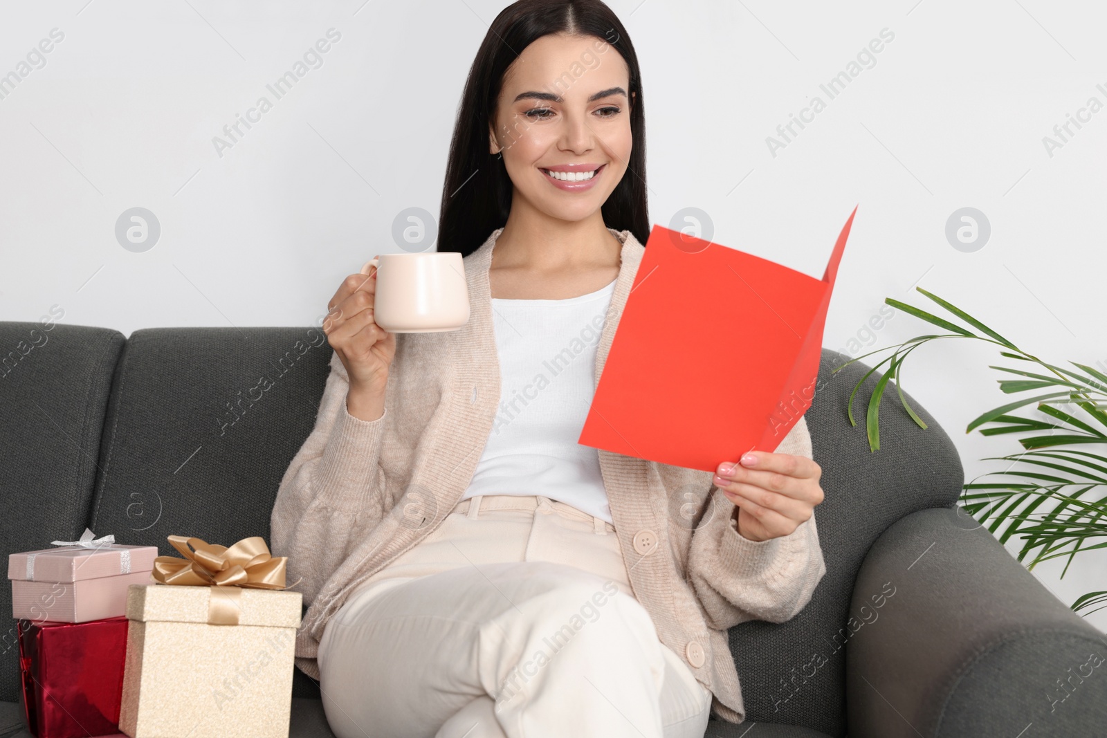 Photo of Happy woman reading greeting card while drinking coffee on sofa in living room