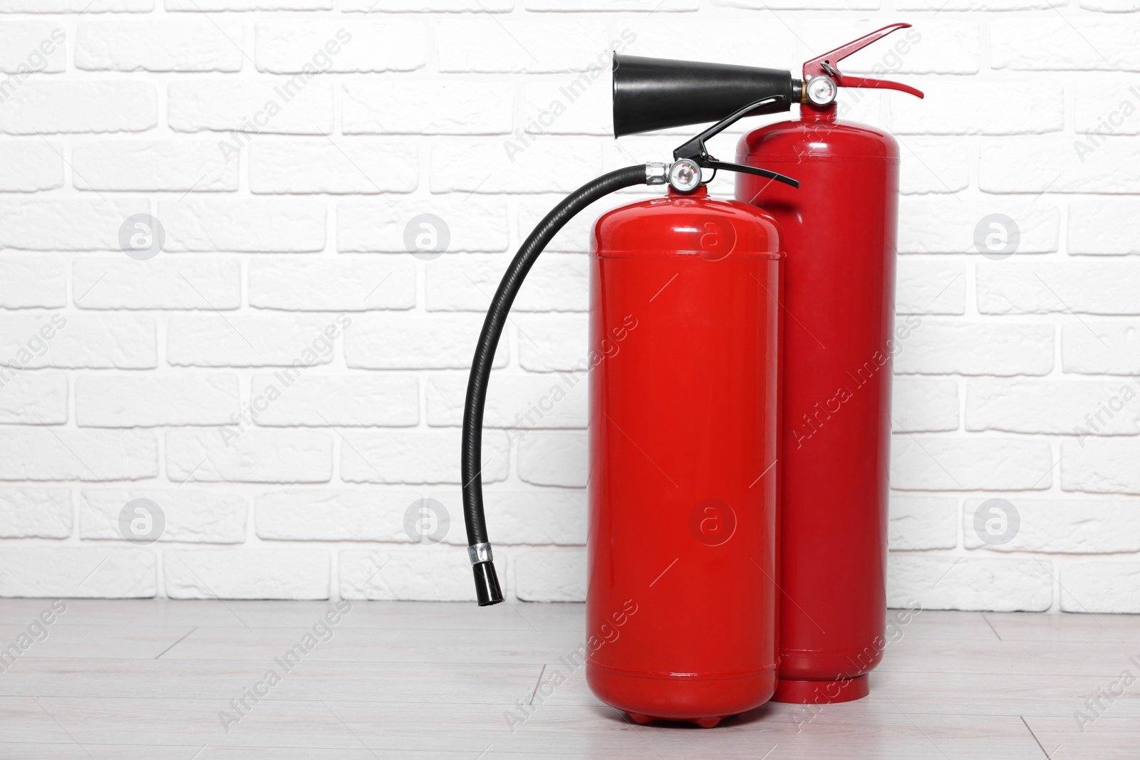 Photo of Red fire extinguishers near white brick wall, space for text